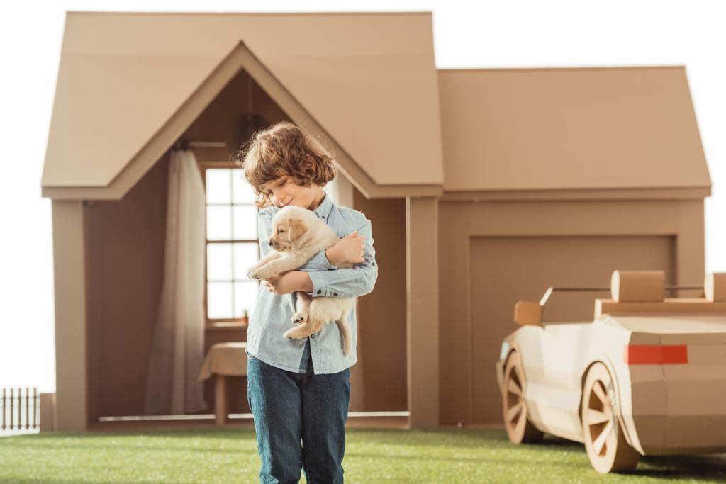 onun çok güzel labrador köpek yavrusu üzerinde beyaz izole karton evin önünde tutan küçük bir çocuk - Fotoğraf, Görsel