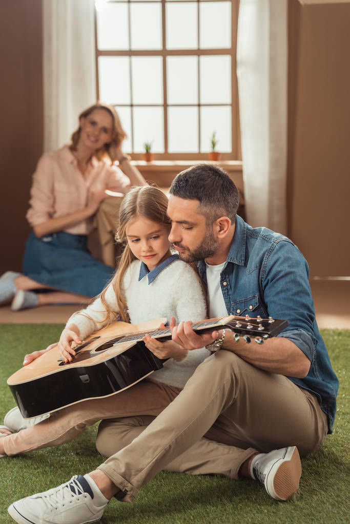 padre e hija tocando la guitarra en la hierba frente a la casa de cartón con la madre sentada dentro
 - Foto, imagen