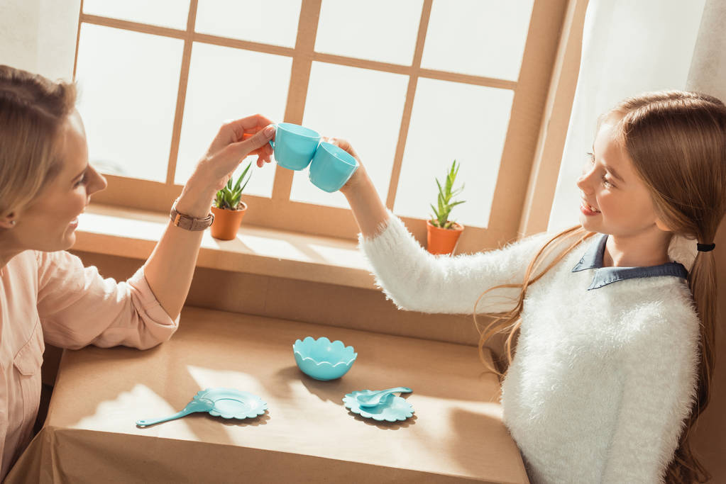 madre e hija teniendo fiesta de té en casa de cartón y tazas de tintineo
 - Foto, Imagen