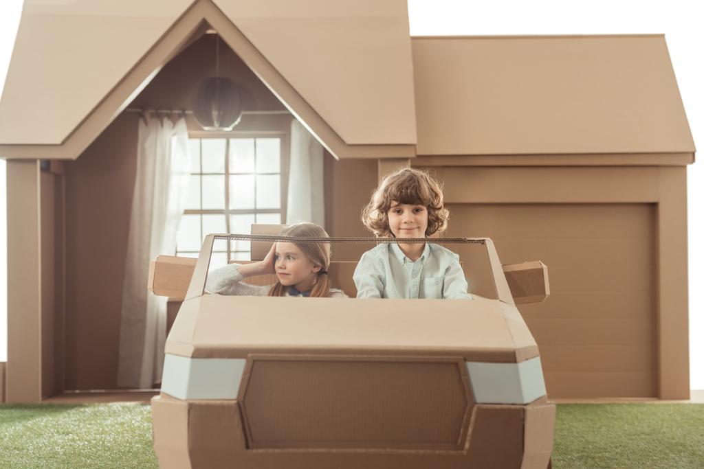 діти їздять на картонному автомобілі перед будинком
 - Фото, зображення
