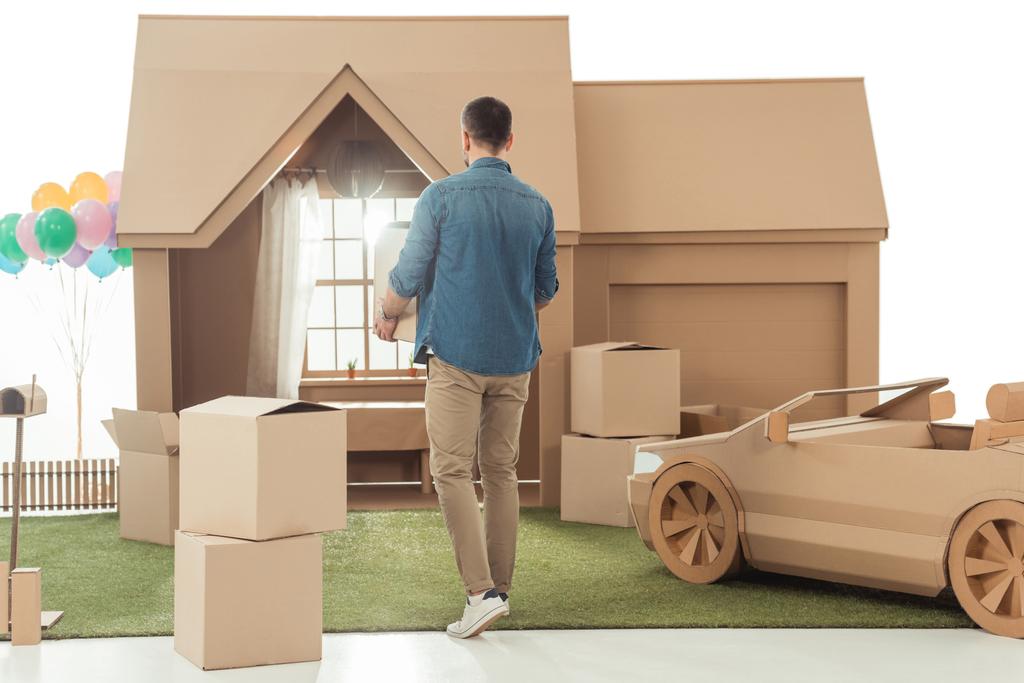 вид ззаду людини з коробками, що переміщуються в новий картонний будинок ізольований на білому
 - Фото, зображення
