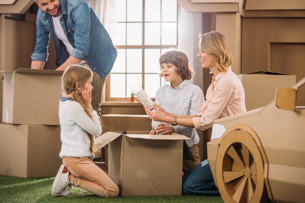 young family unpacking boxes while moving into new cardboard house - Photo, Image