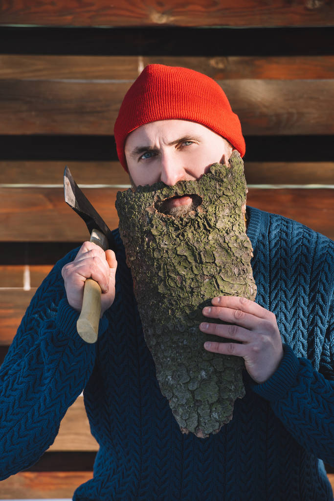 портрет человека с бородой из древесной коры и топором в руке на открытом воздухе
 - Фото, изображение