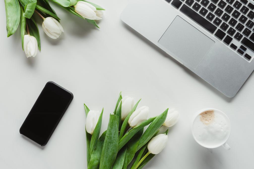 flache Liege mit Kaffeetasse, Laptop, Smartphone und weißen Tulpen auf weißer Oberfläche - Foto, Bild