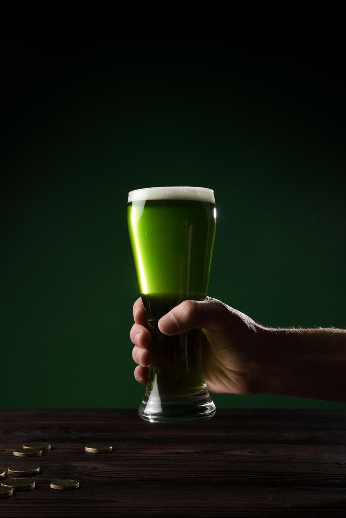 bijgesneden afbeelding van man met glas groene bier boven tafel met munten, st patricks dag concept - Foto, afbeelding