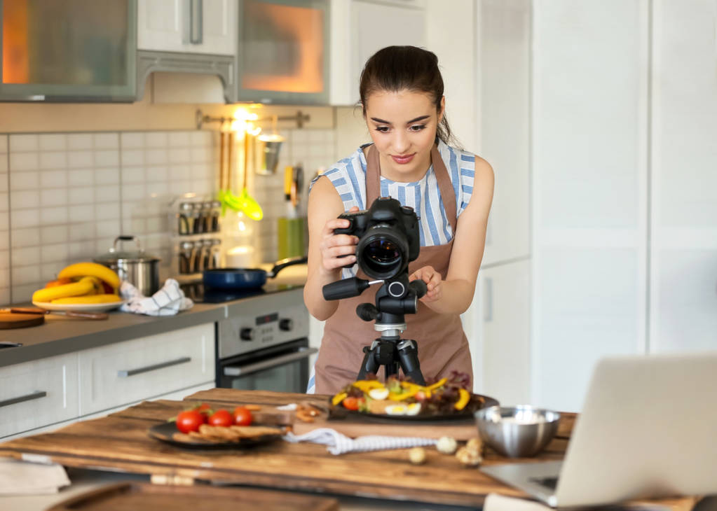 Молодая женщина с профессиональной камерой делает натюрморты фотографии на кухне
 - Фото, изображение