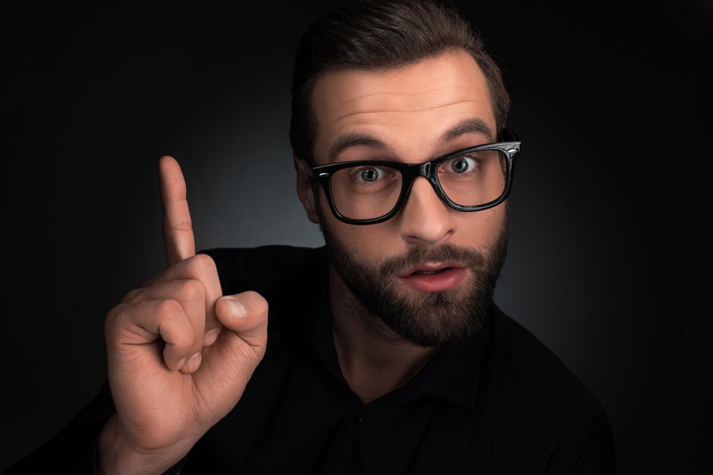 Porträt eines Mannes mit Brille, der isoliert auf schwarz zeigt - Foto, Bild