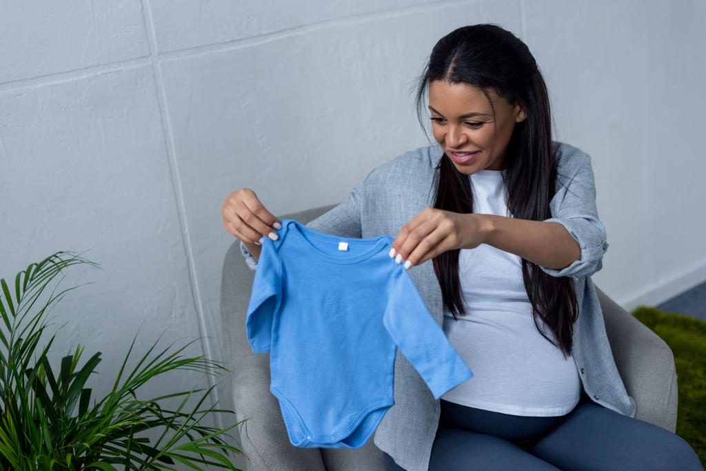 afro-amerikai terhes nő tartja a baba kék Body karosszékben ülve - Fotó, kép