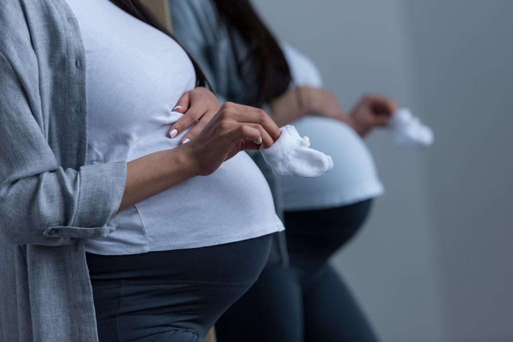 vista recortada de la mujer embarazada sosteniendo pequeños calcetines en el espejo
 - Foto, Imagen