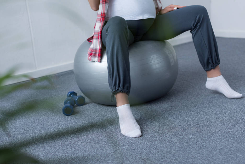 rajattu näkymä raskaana istuva nainen kunnossa pallo käsipainoilla lähellä
 - Valokuva, kuva