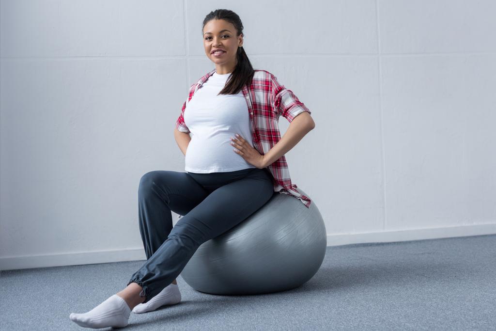 フィット ボールの上に座って満足しているアフリカ系アメリカ人の妊娠中の女性 ロイヤリティフリー写真 画像素材