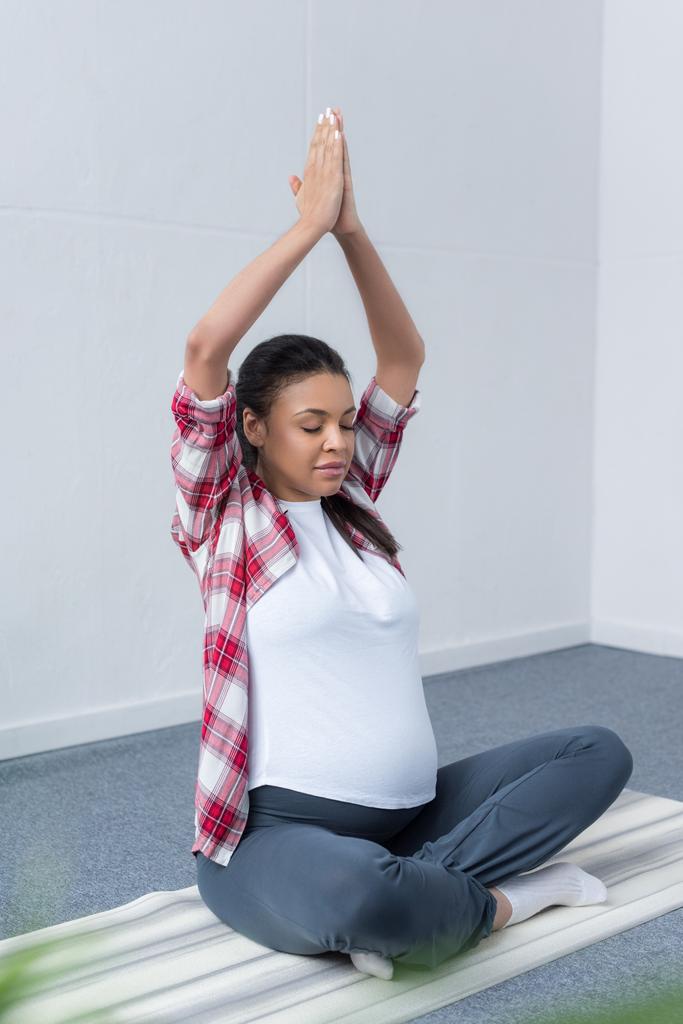 africaine américaine enceinte femme méditant avec les yeux fermés et namaste mudra sur tapis de yoga
  - Photo, image