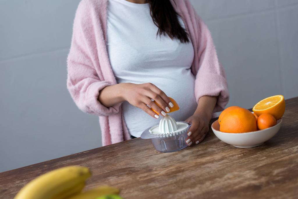 vista parziale della donna incinta che produce succo d'arancia con spremiagrumi
 - Foto, immagini