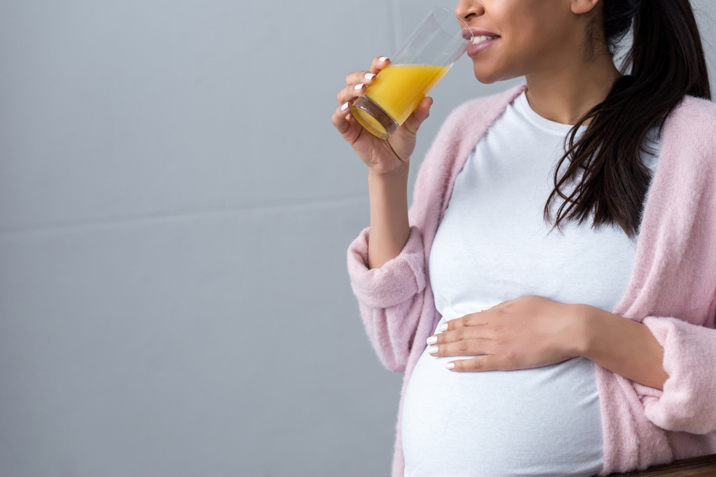 オレンジ ジュースを飲んで妊娠中のアフリカ系アメリカ人の女性観をトリミング  - 写真・画像