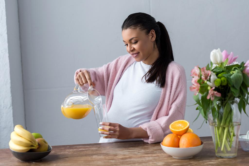 afro-américaine enceinte verser du jus à la cuisine avec des fruits frais
 - Photo, image