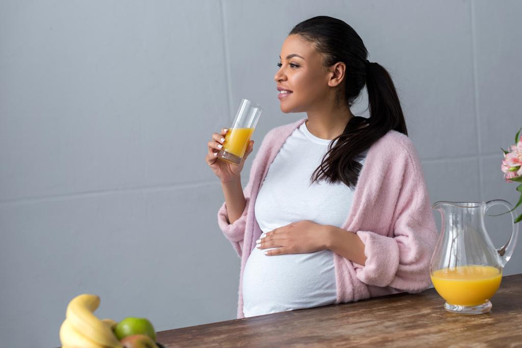 hamile kadınla Afro-Amerikan cam mutfak at portakal suyu - Fotoğraf, Görsel