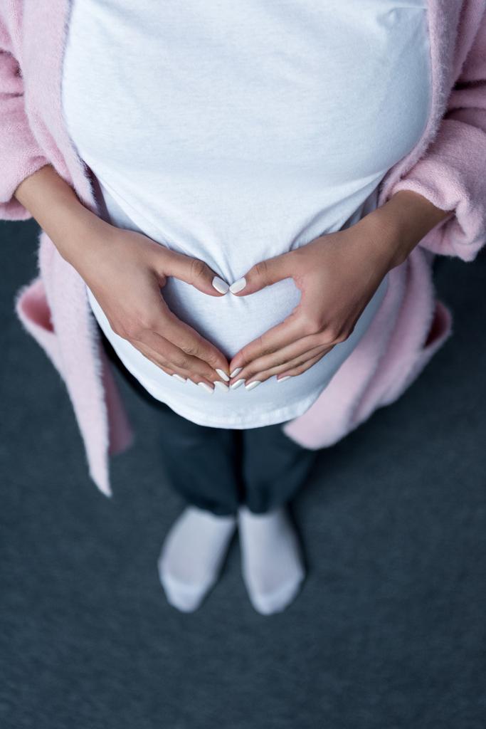 vista ritagliata della donna incinta che fa il simbolo del cuore con le mani sulla pancia
 - Foto, immagini