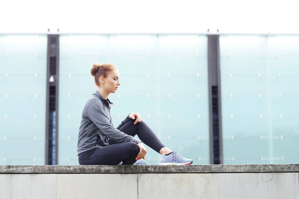 Jong, passen en sportieve vrouw zittend op de betonnen rand. Fitness, sport, stedelijke joggen en gezonde levensstijl concept. - Foto, afbeelding