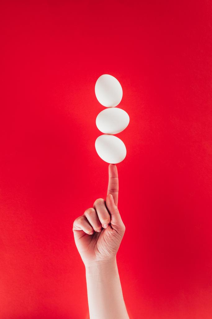 vista parcial de la mujer sosteniendo huevos de gallina crudos levitantes en el dedo aislado en rojo
 - Foto, Imagen