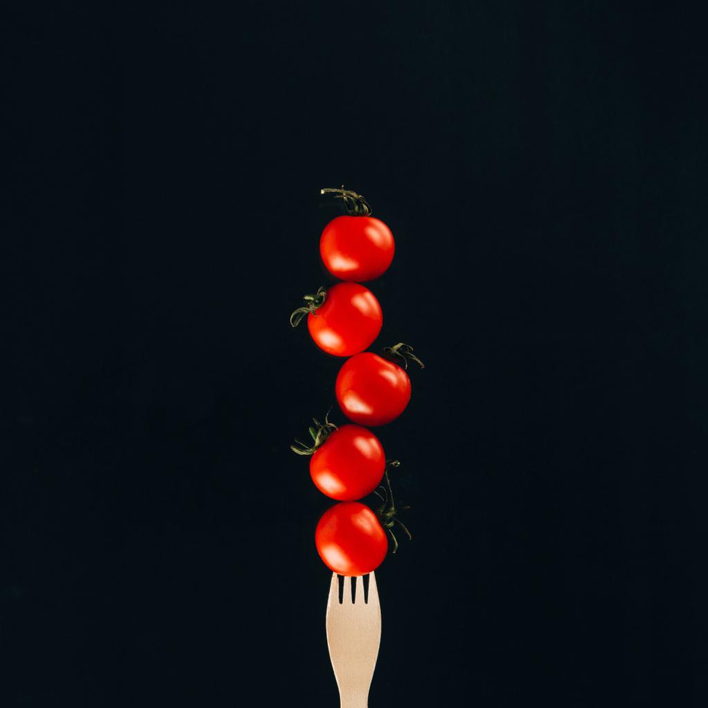 Close-up van zwevende cherry tomaten op vork geïsoleerd op zwart - Foto, afbeelding