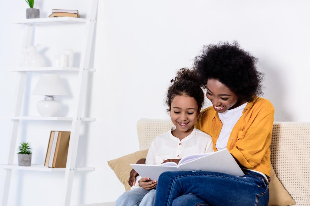 щаслива афроамериканська мати і дочка читають книгу разом вдома
 - Фото, зображення
