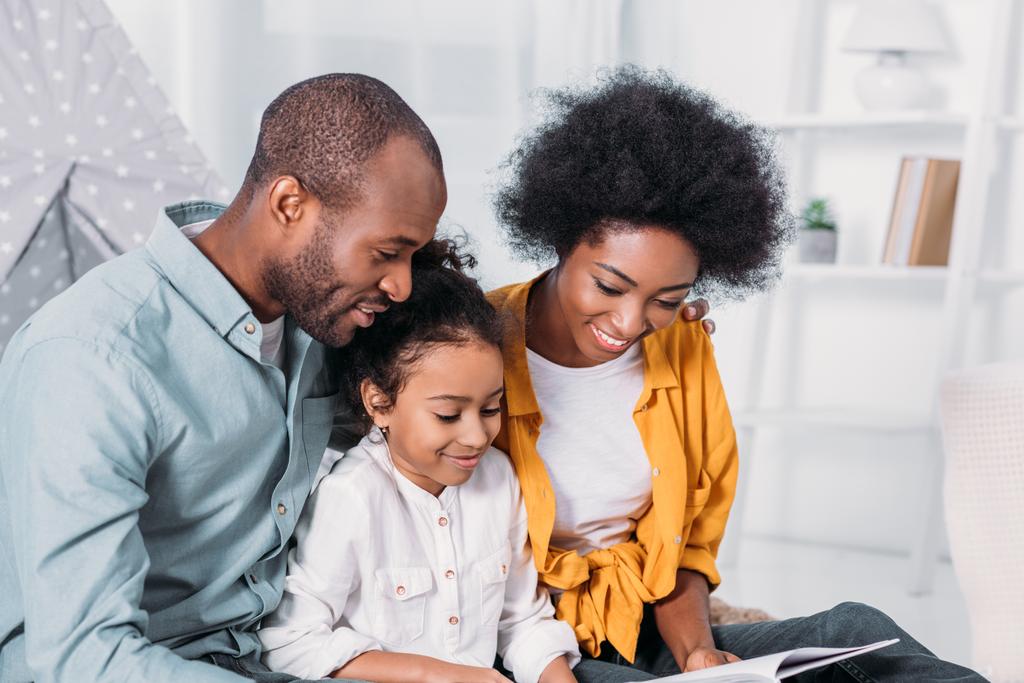 padres afroamericanos leyendo con su hija en casa
 - Foto, Imagen