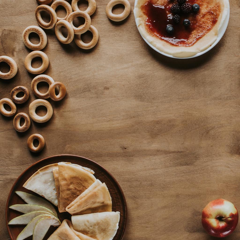 bovenaanzicht van lekkere huisgemaakte pannenkoeken met jam en bessen, appel en bagels op houten tafel - Foto, afbeelding