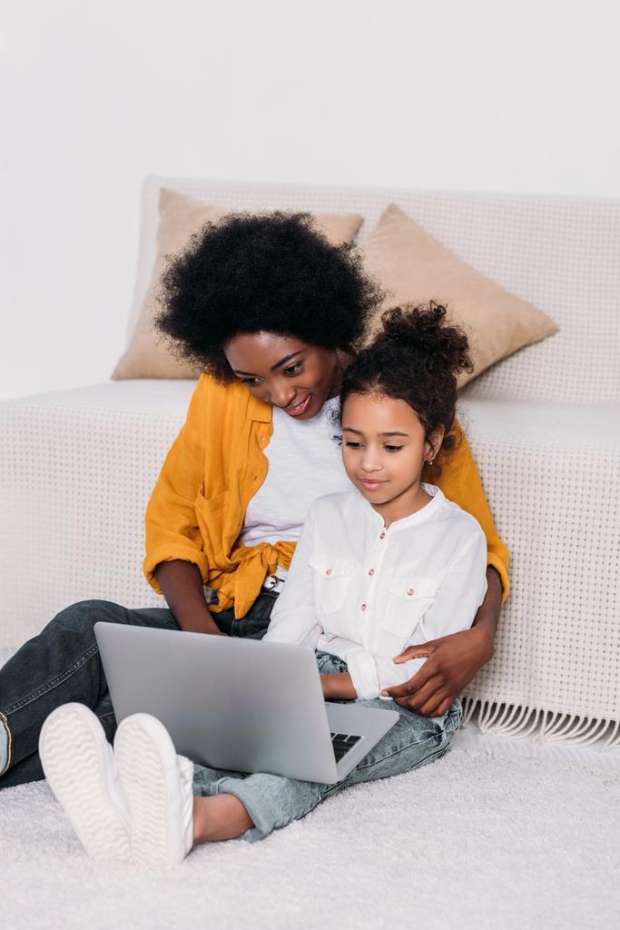 madre afroamericana y su hija abrazando y viendo algo en el portátil
 - Foto, imagen