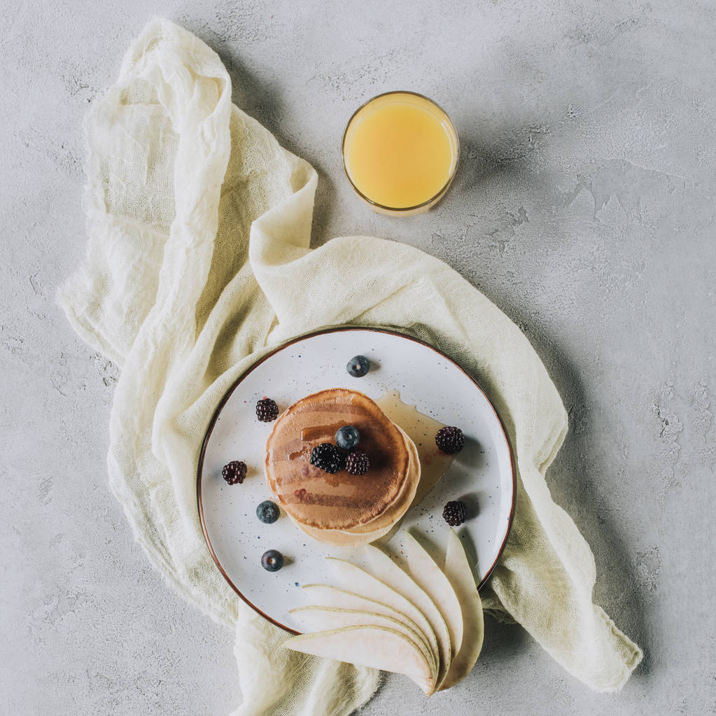 bovenaanzicht van heerlijke huisgemaakte pannenkoeken met vers fruit en een glas sap op grijs - Foto, afbeelding