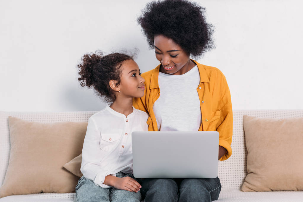 Африканская американская мать и дочь с ноутбуком на диване дома
 - Фото, изображение