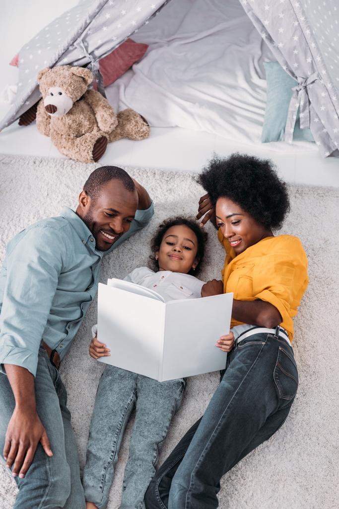 vysoký úhel pohled na africké americké rodiče a dcera leží na podlaze a čtení knihy - Fotografie, Obrázek