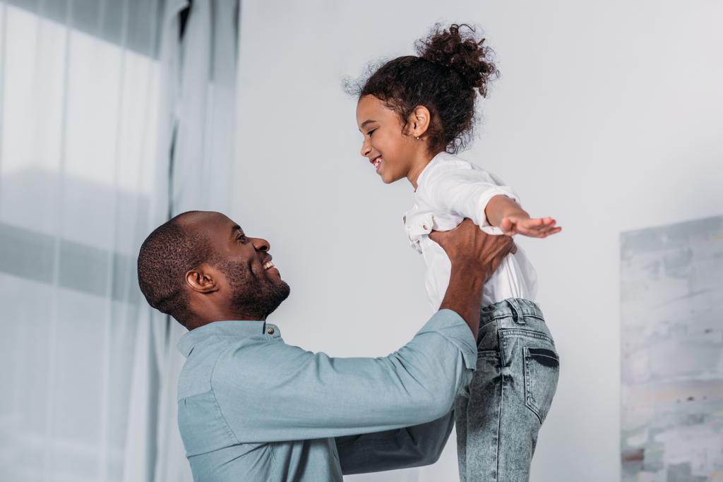 happy african american father raising daughter at home - Photo, Image