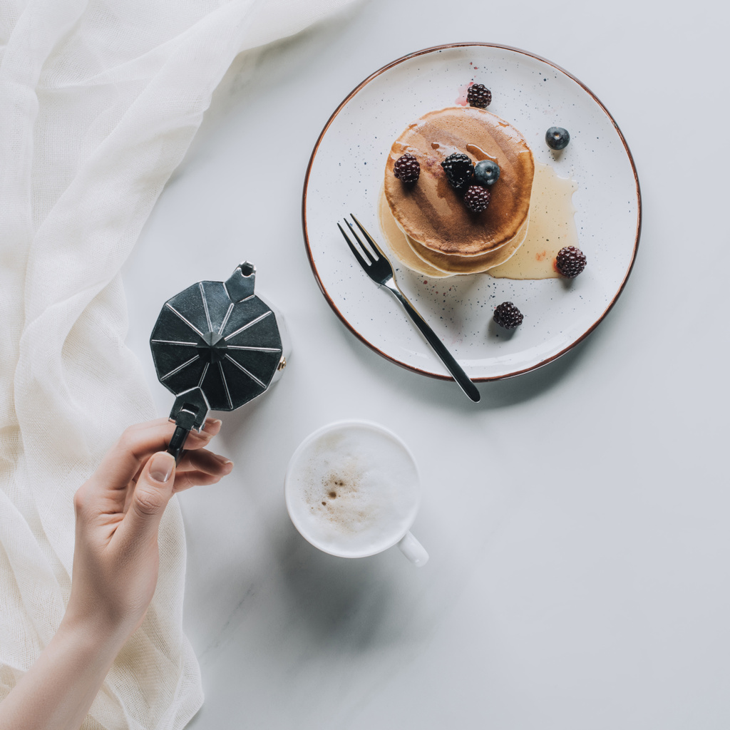 top view of person holding coffee pot while eating sweet pancakes with berries for breakfast - Photo, Image