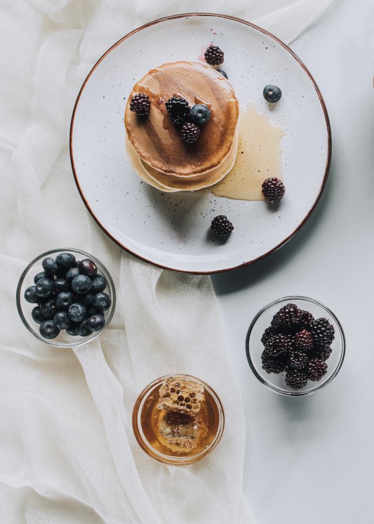 top view of tasty homemade pancakes with honey, blueberries and blackberries on grey - Photo, Image