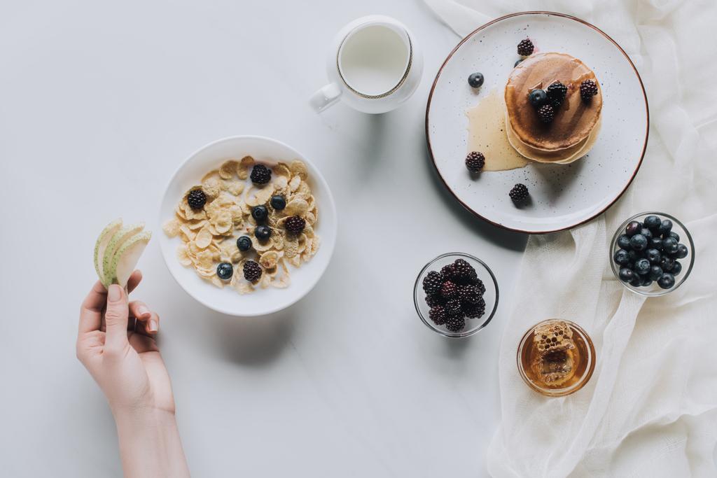 inyección recortada de la persona que come muesli saludable y panqueques con frutas para el desayuno en gris
 - Foto, imagen