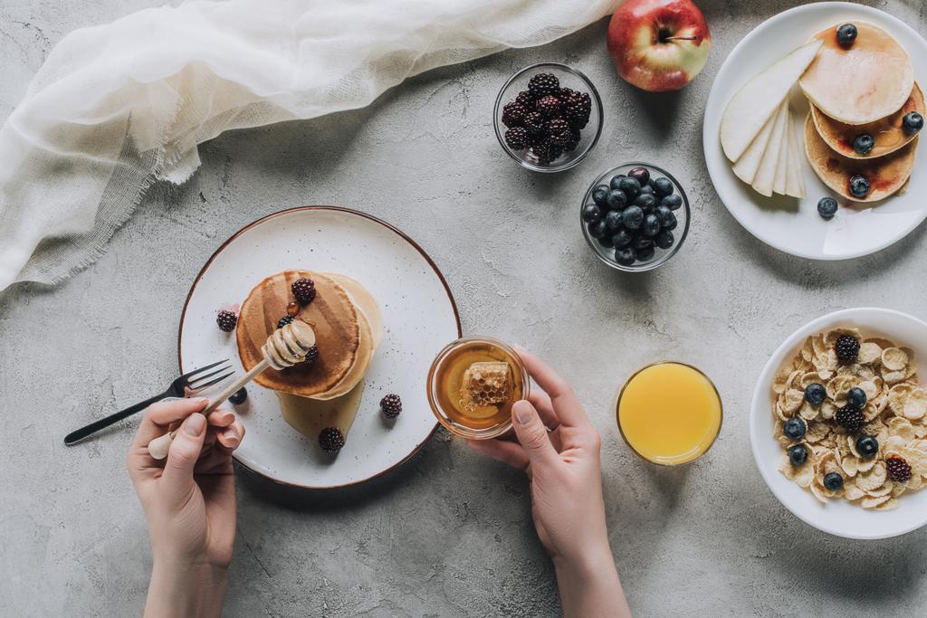 обрізаний знімок людини, що їсть смачні домашні млинці з медом та фруктами на сірому
 - Фото, зображення