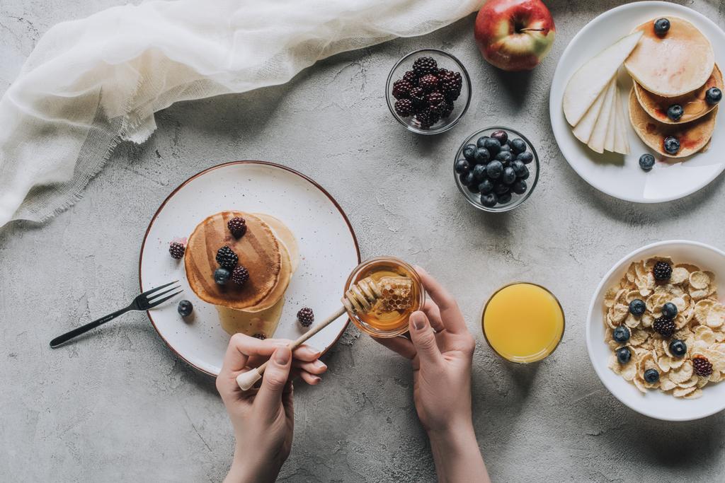 top view of person eating delicious homemade pancakes with honey and fruits on grey - Photo, Image