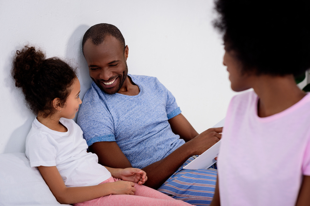 χαμογελώντας αφρικανικές αμερικανικές γονείς και κόρη βλέπουν κάθε άλλο στο σπίτι - Φωτογραφία, εικόνα