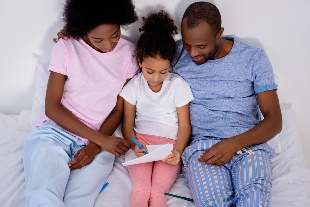 genitori afroamericani aiutare figlia pittura in album a letto a casa
 - Foto, immagini