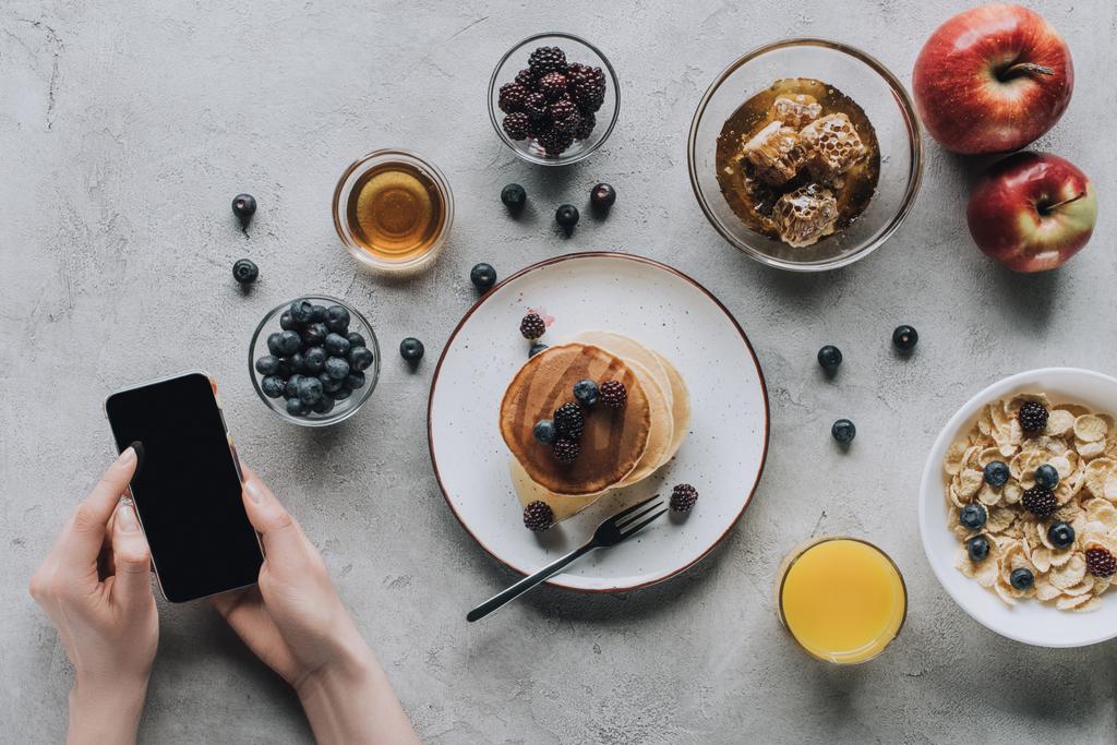 обрезанный снимок человека с помощью смартфона во время здорового вкусного завтрака
 - Фото, изображение