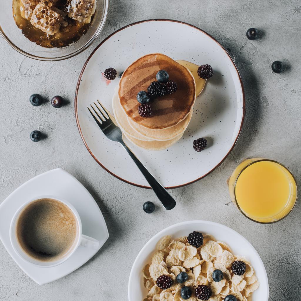 top view of sweet pancakes with berries, juice, honey, muesli and coffee on grey - Photo, Image