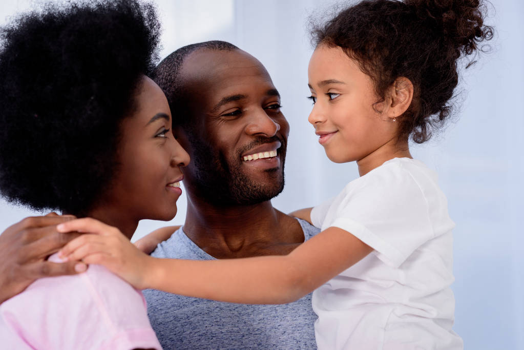 afro-amerikai szülők és a lánya, átölelve és néztek egymásra, otthon - Fotó, kép