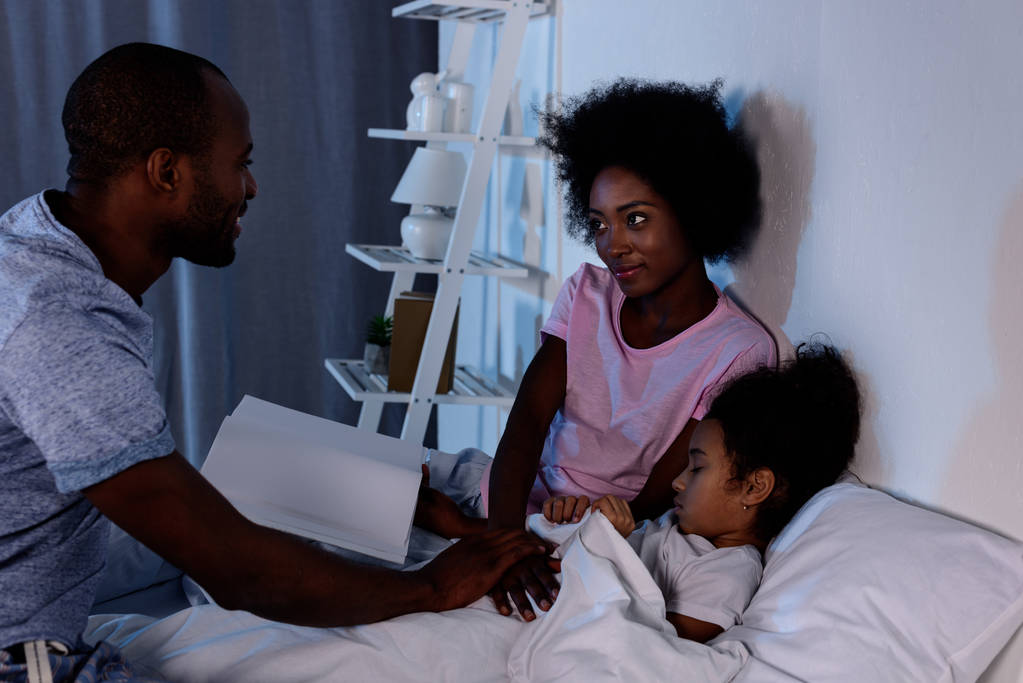afro-amerikai szülők könyv és lánya az ágyban - Fotó, kép