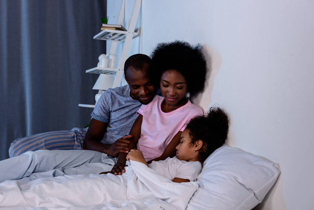 afroamericanos padres mirando durmiendo hija
 - Foto, imagen