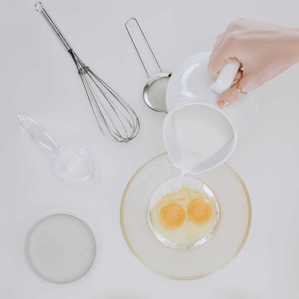 bovenaanzicht van persoon gieten melk tijdens het koken van pannenkoeken geïsoleerd op grijs  - Foto, afbeelding