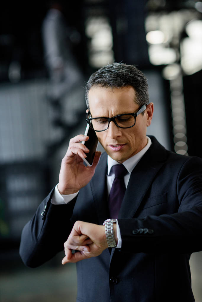 retrato del hombre de negocios comprobando el tiempo mientras habla en el teléfono inteligente
 - Foto, Imagen