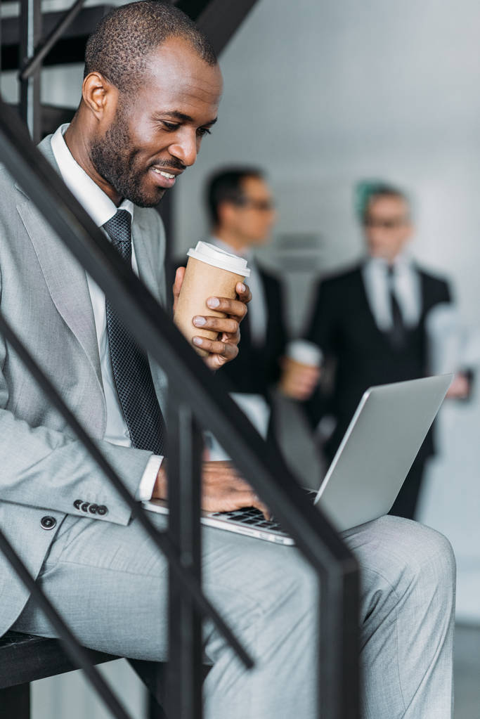 Selektywny fokus uśmiechnięta Afroamerykanin z kawa na wynos biznesmen pracy na laptopie - Zdjęcie, obraz