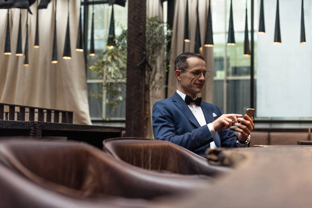 schöner Mann im schicken Anzug mit Smartphone im Restaurant - Foto, Bild