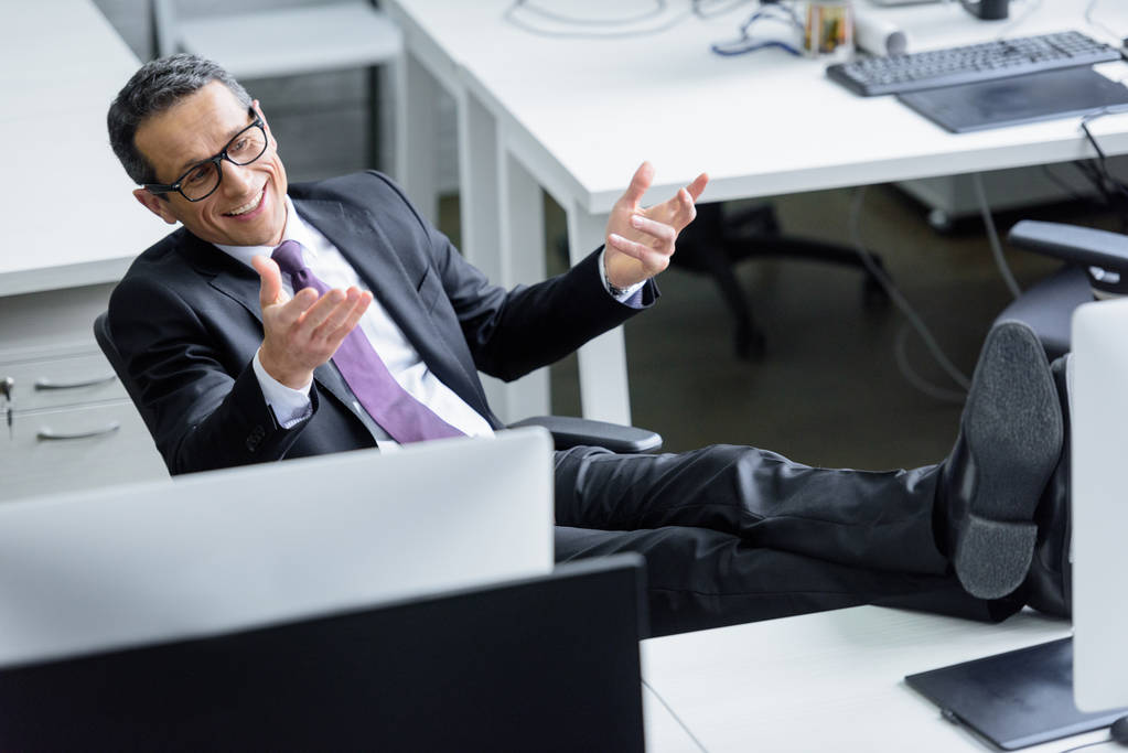 веселый бизнесмен в очках сидит на рабочем месте в офисе
 - Фото, изображение