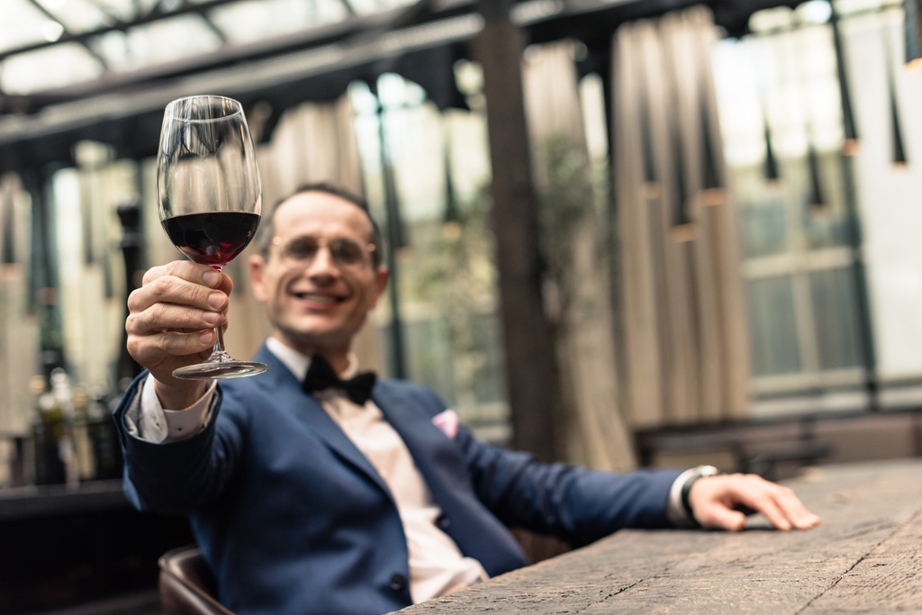przystojny mężczyzna w szykowny garnitur z kieliszek czerwonego wina w restauracji - Zdjęcie, obraz